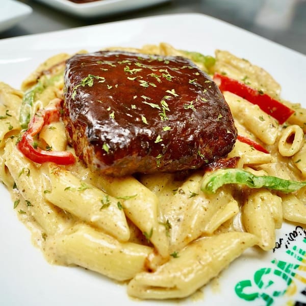 Island Tings' Jamaican jerk chicken pasta, topped with a rich brown sauce and fresh herbs.