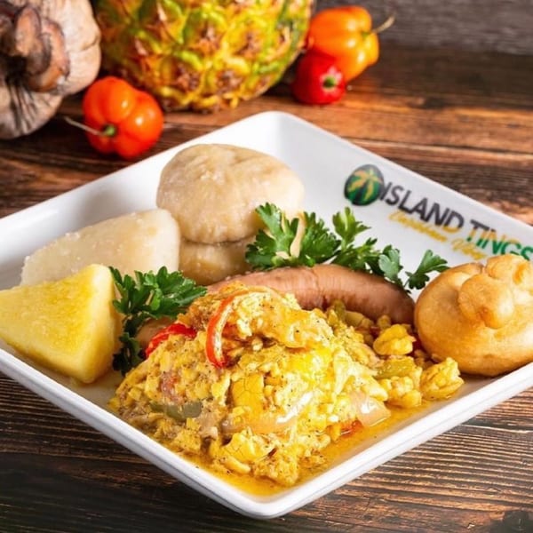 A Jamaican breakfast platter with ackee and saltfish, boiled dumplings, fried dumplings, and sausage.