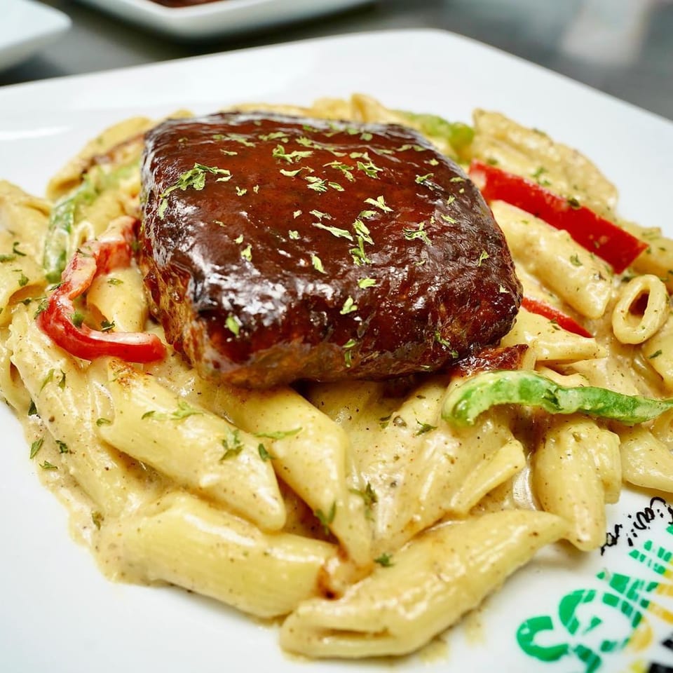 A Jamaican dish of penne pasta with creamy sauce, bell peppers, and a large piece of jerk meat.