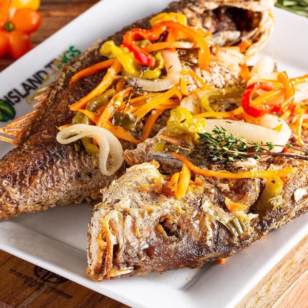 Two whole fried Jamaican escovitch fish topped with colorful peppers, onions, and thyme on a white plate.