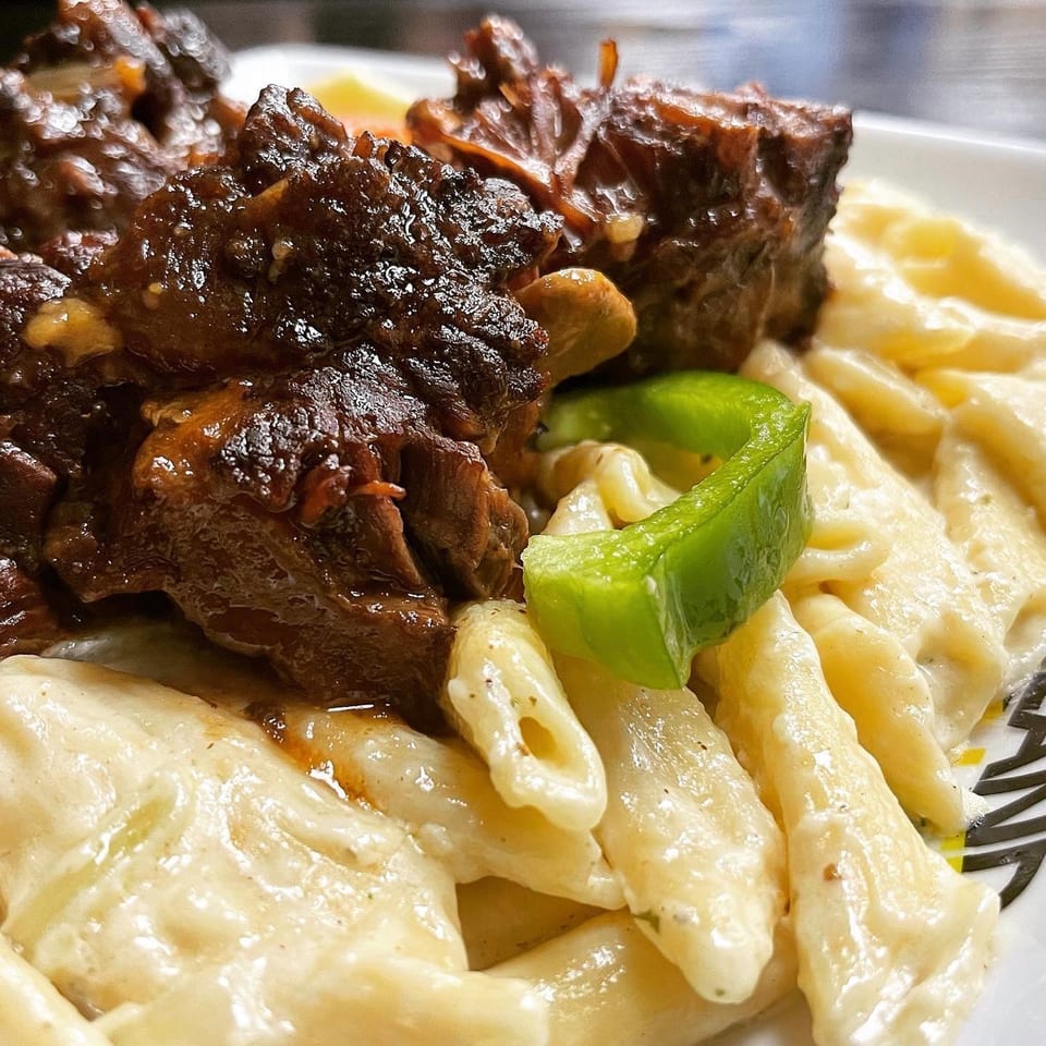 Island Tings' Jamaican oxtail stew with creamy penne pasta and a green bell pepper garnish.