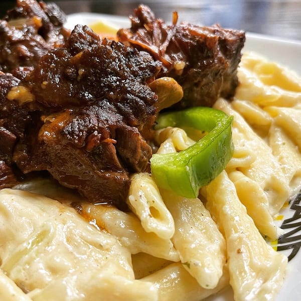 Island Tings' Jamaican oxtail stew with creamy penne pasta and a green bell pepper garnish.