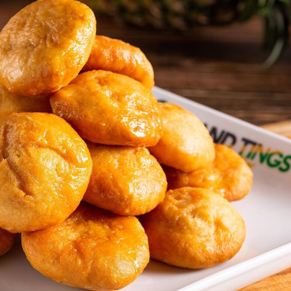 A white rectangular plate filled with golden-brown, glistening Jamaican festival dumplings from Island Tings.