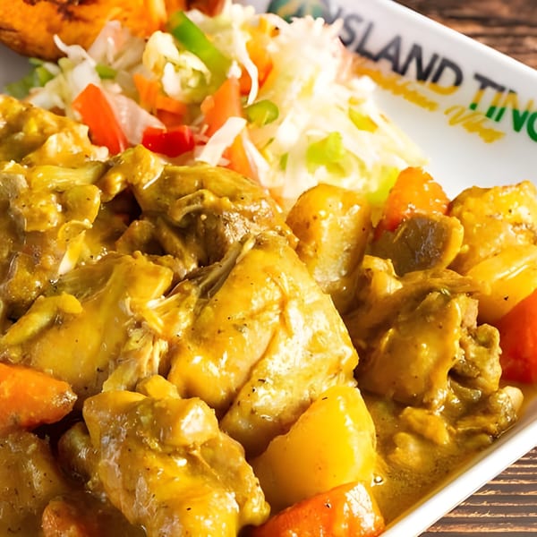 Close-up of Jamaican curry chicken with potatoes and carrots, served with coleslaw on an Island Tings plate.